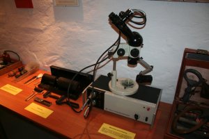 Na stole stoi mikroskop stereoskopowy z lat siedemdziesiątych produkcji Państwowych Zakładów Optycznych w Warszawie.