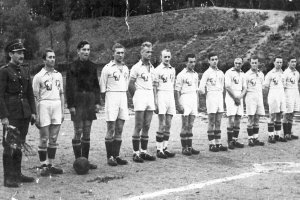 Drużyna piłkarzy przed rozpoczęciem meczu. Mężczyźni stoją wzdłuż linii środkowej boiska.
